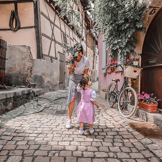 Carolina Fryer plays with her daughter on a cobblestone street while holding a plant